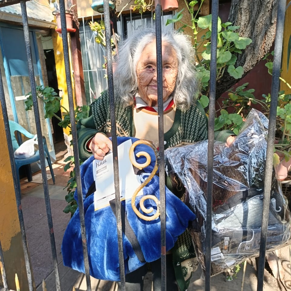 Adulta mayor recibiendo ropa de abrigo en la puerta de su casa